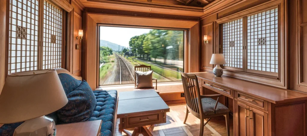 DX Suite du Seven Stars in Kyushu &mdash; salon avec canap&eacute; et fen&ecirc;tre panoramique donnant sur la voie ferr&eacute;e et les paysages de Kyushu