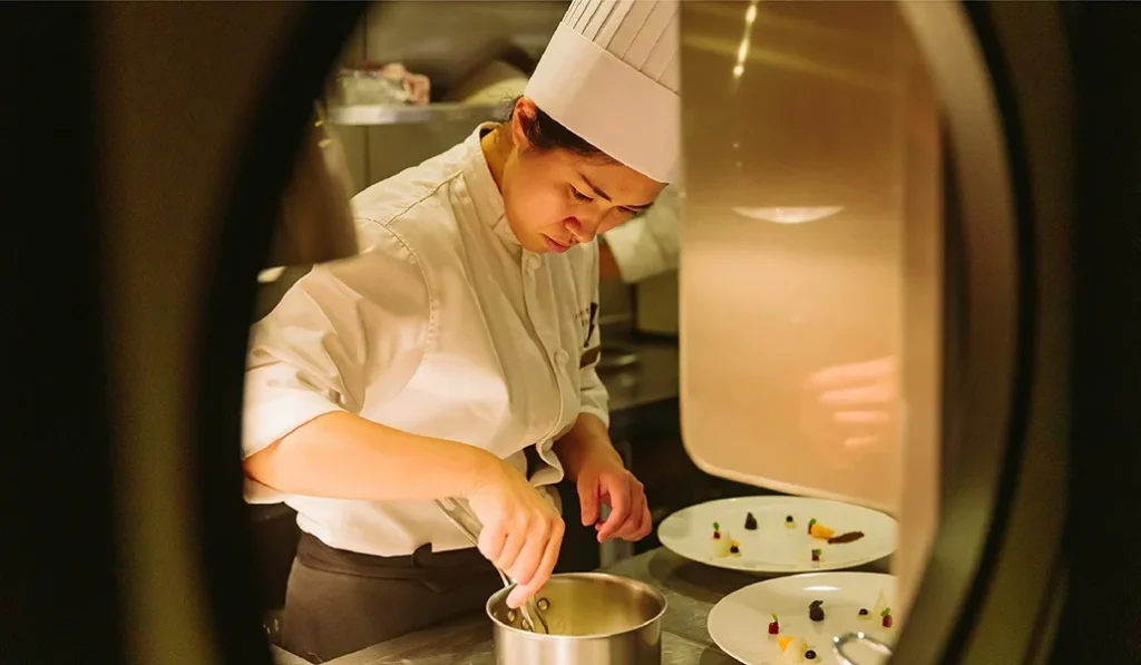 Chef du Twilight Express Mizukaze pr&eacute;parant un plat gastronomique dans la cuisine du wagon-restaurant Pleiades