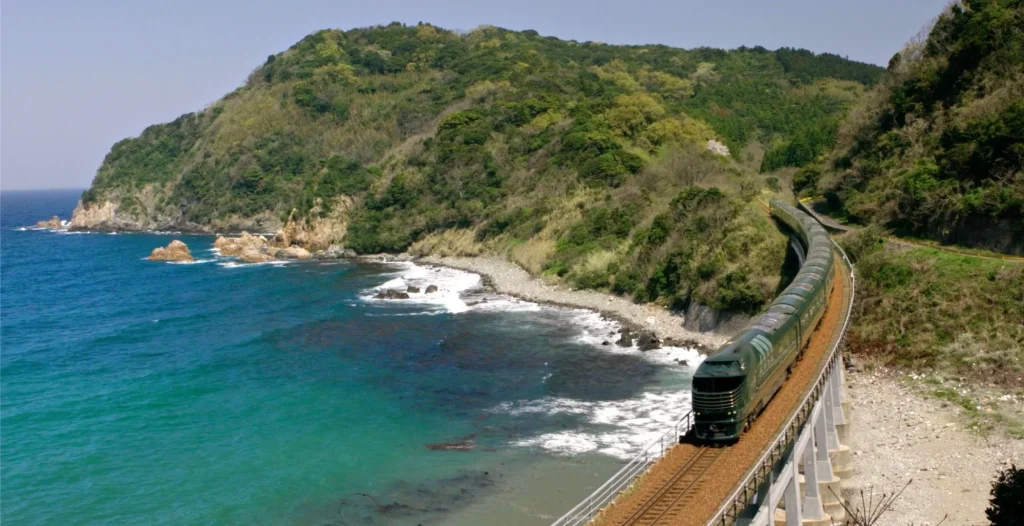 Train de luxe Twilight Express Mizukaze longeant la c&ocirc;te rocheuse de San'in face &agrave; l'oc&eacute;an turquoise